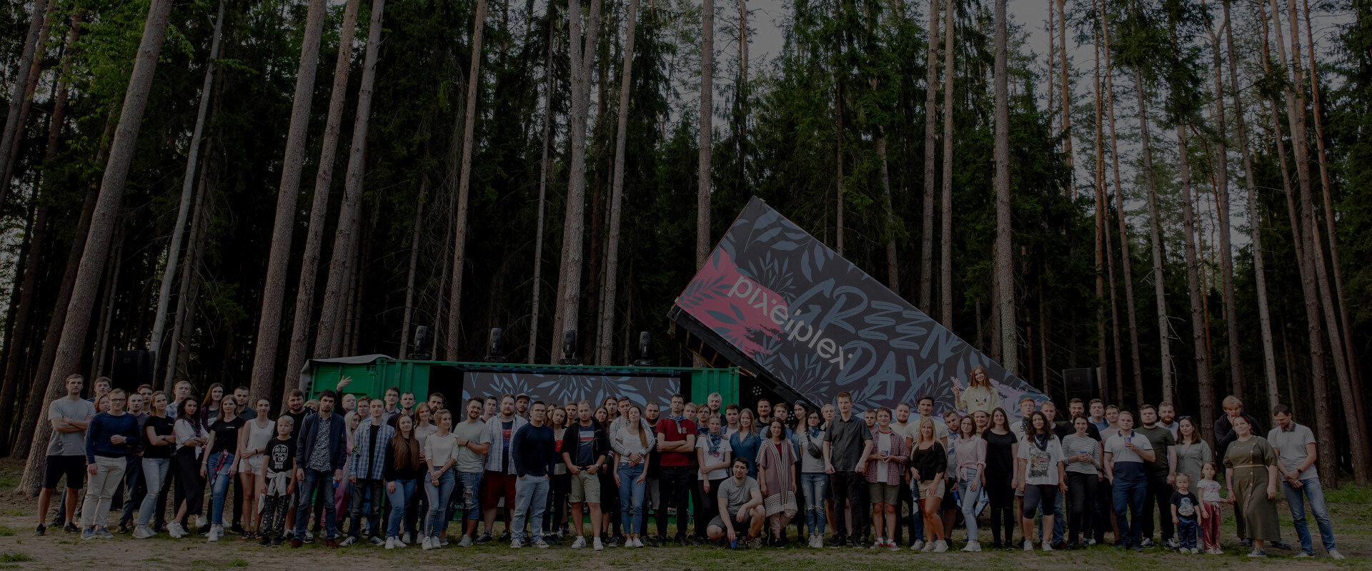 Панорамное фото сотрудников, которые стоят на фоне логотипа PixelPlex и лесного массива