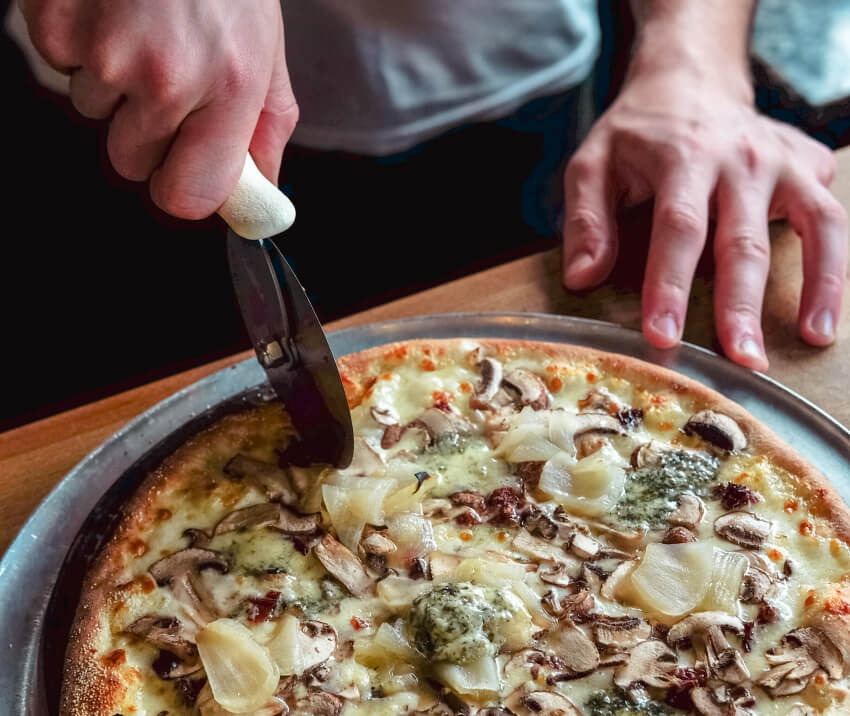 Человек разрезает пиццу с помощью ножа для пиццы